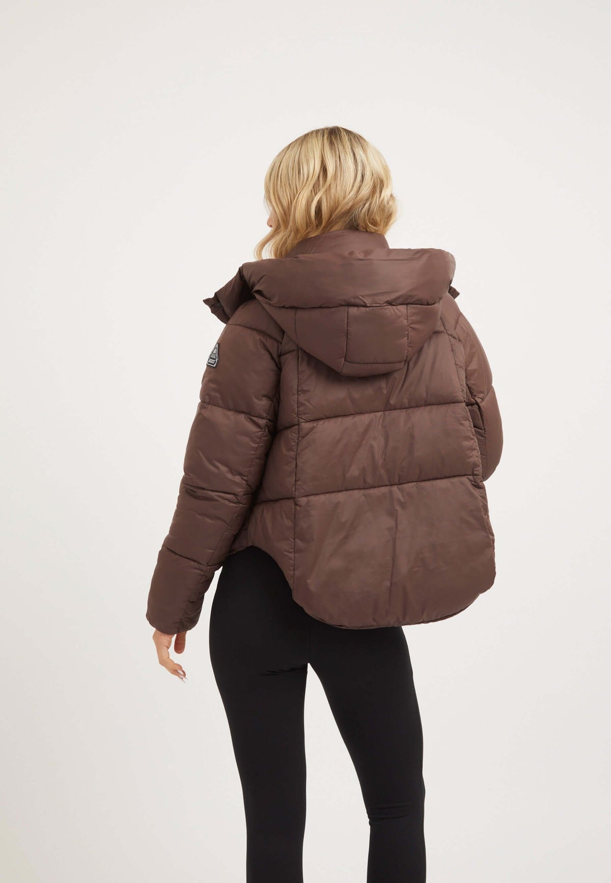 Back view of a woman wearing a mid brown short puffer jacket women with an adjustable hood and modern cropped cut.