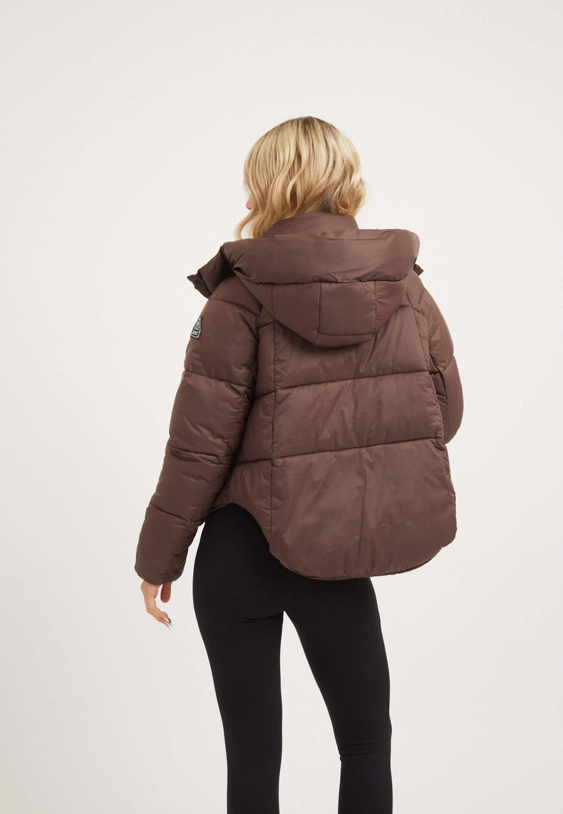Back view of a woman wearing a mid brown short puffer jacket women with an adjustable hood and modern cropped cut.