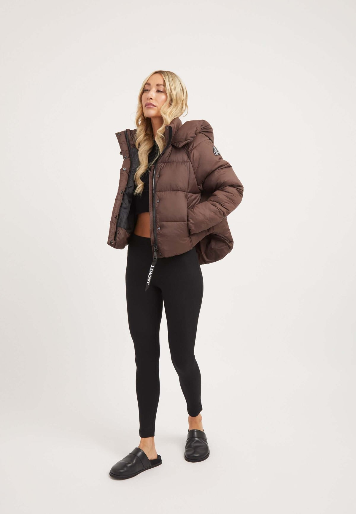 Short puffer jacket women in mid brown cropped style, paired with black leggings and a crop top.
