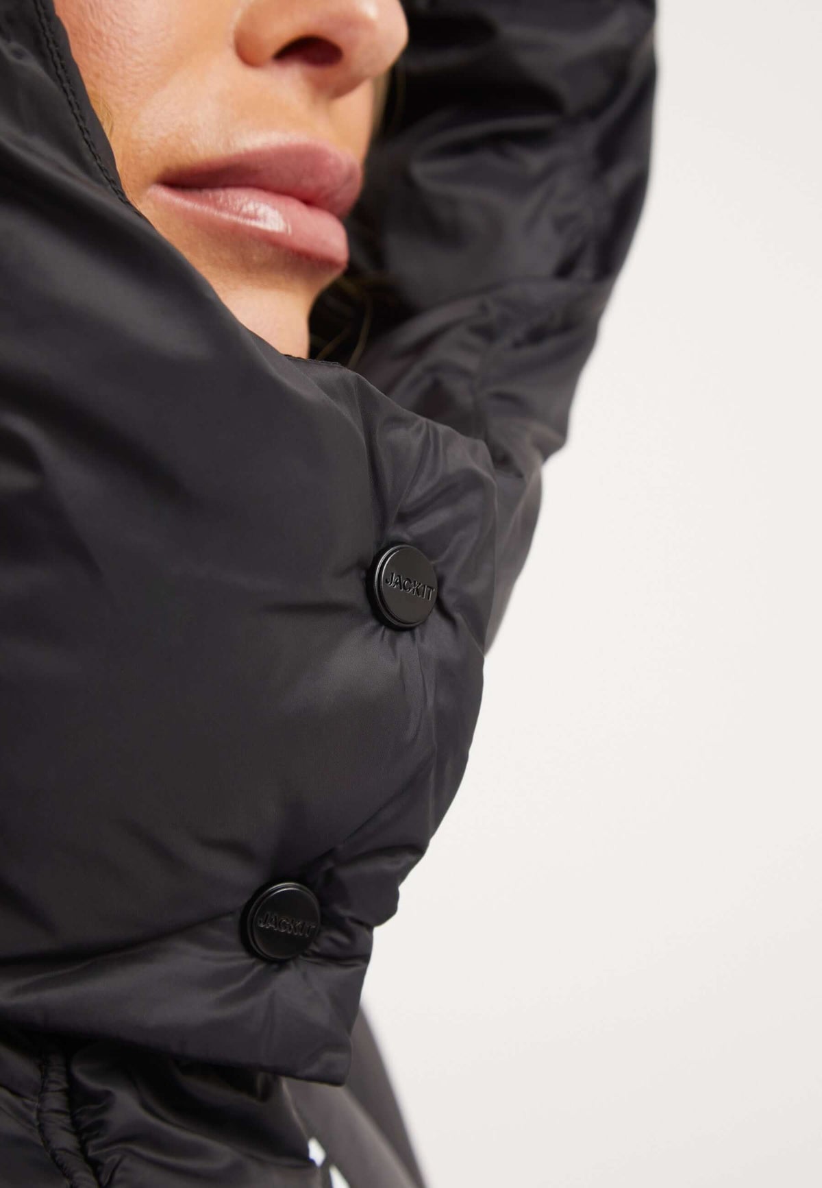 Close-up of a woman's face wearing the Cloud Crop Jacket Black showing the adjustable hood and buttons, highlighting the womens short puffer jacket.