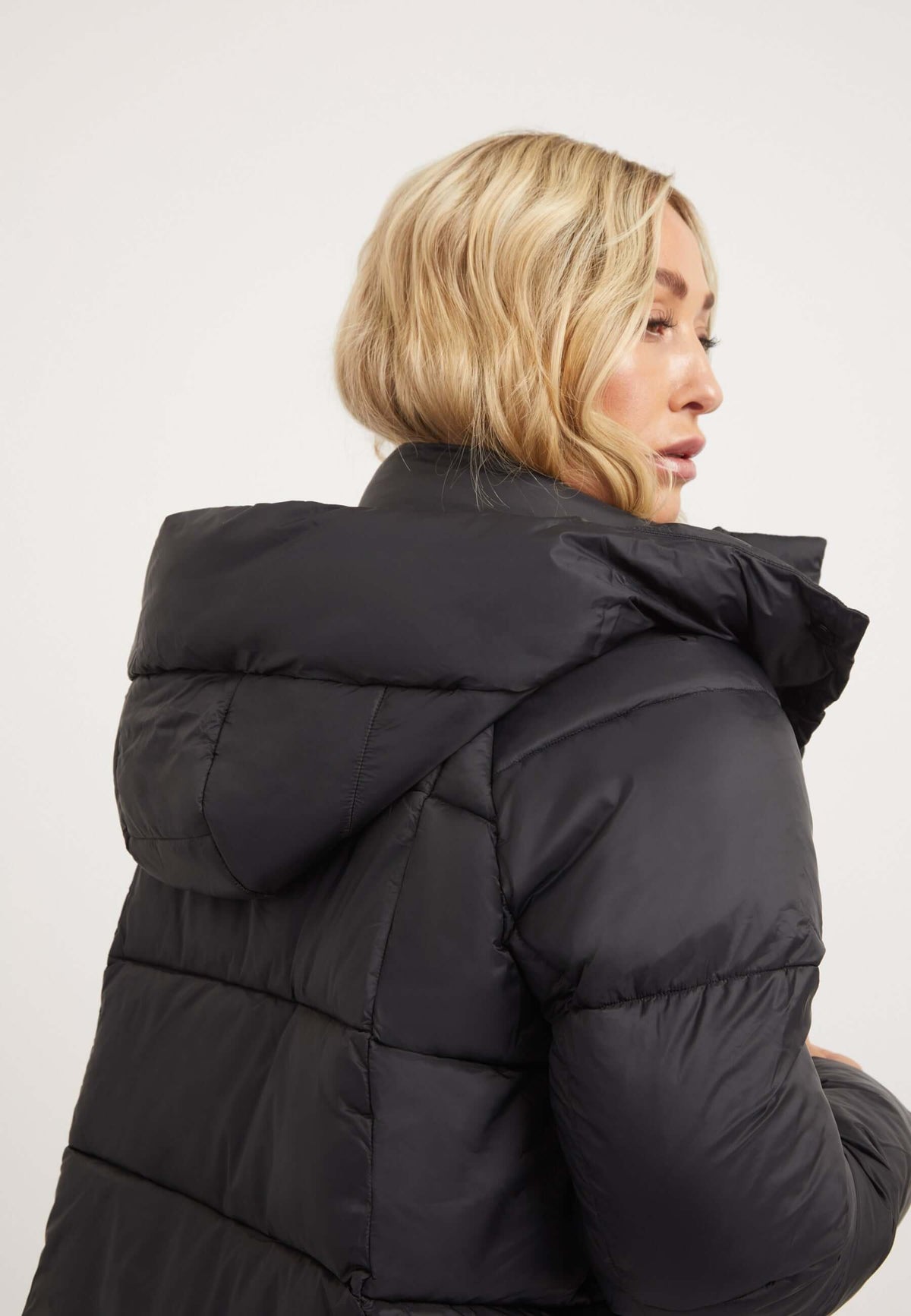 Rear view of a woman wearing a black Cloud Crop Jacket, showcasing the stylish design of this womens short puffer jacket.