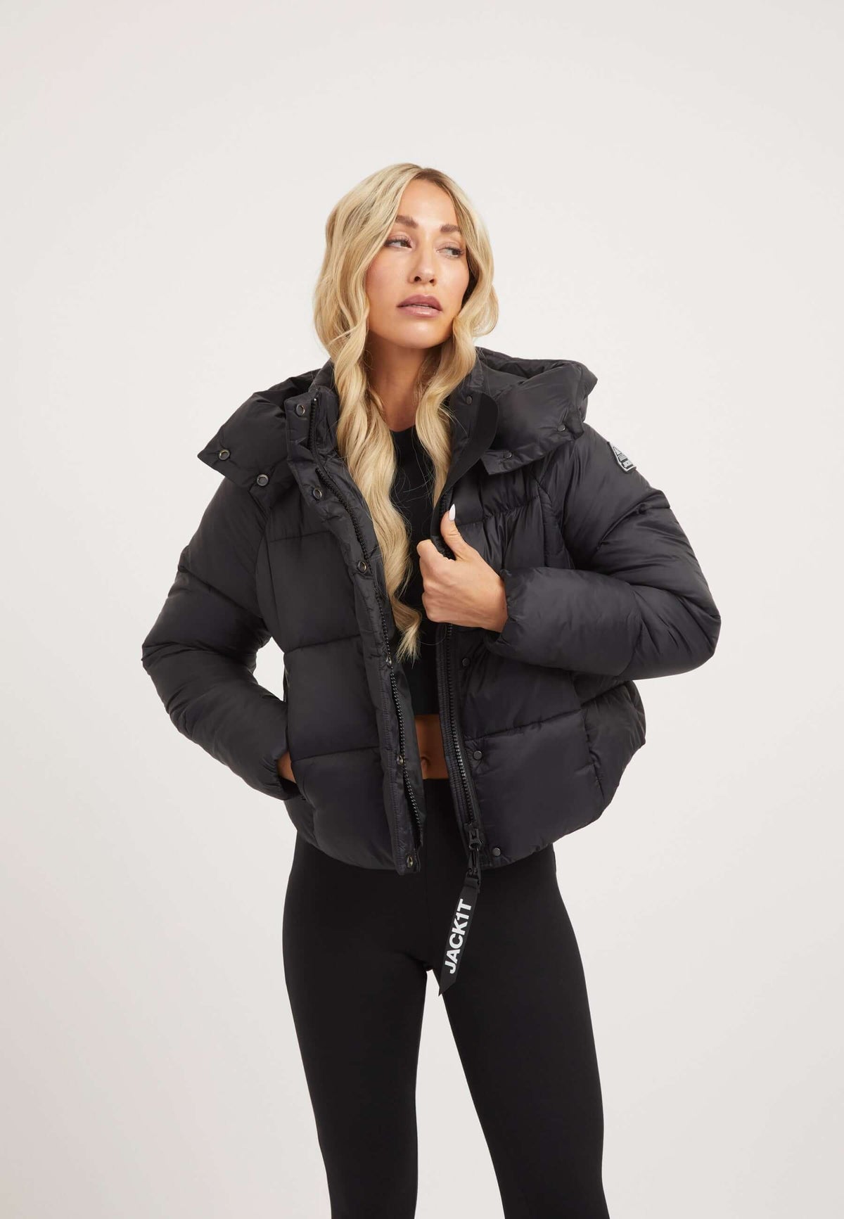 Model wearing a womens short puffer jacket in black with a cropped cut and adjustable hood.