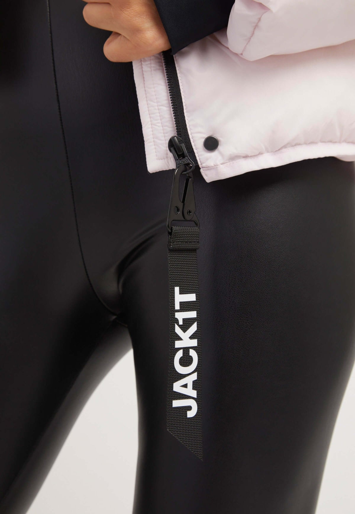 Close-up of the Helio Crop Duvet Jacket in soft pink, featuring adjustable hood and JACK1T tag, paired with black leggings. Short puffer jacket women.