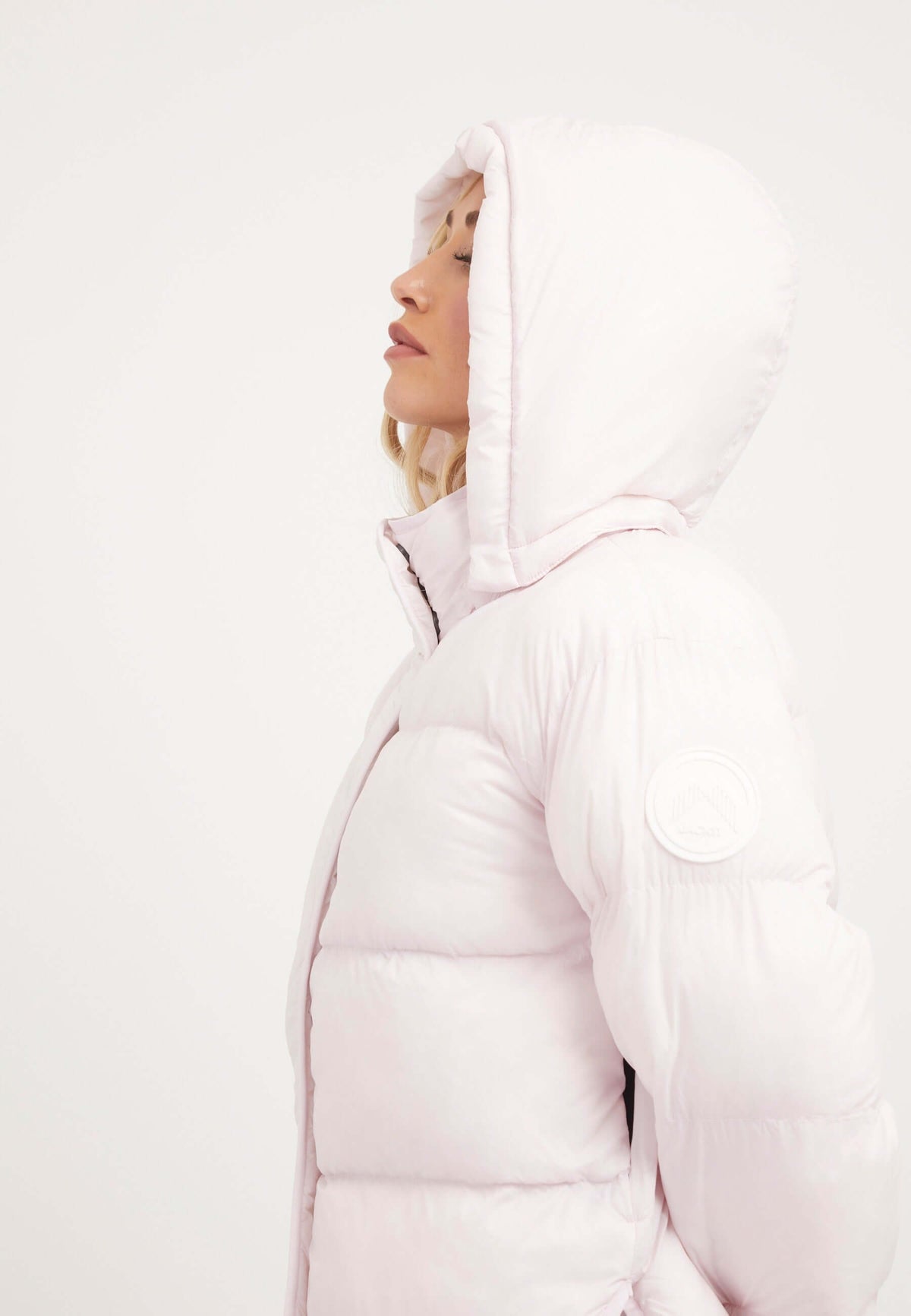 Side view of a model wearing a Helio Crop Duvet Jacket in soft pink, showcasing its stylish cropped design and adjustable hood. Short puffer jacket women.
