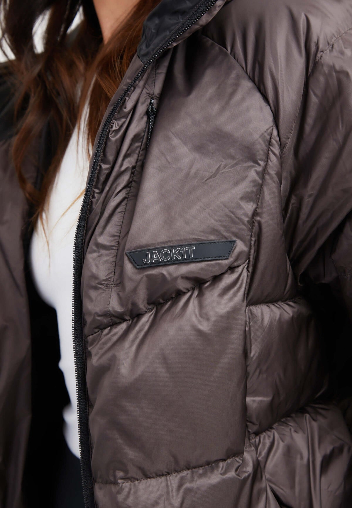 Close-up of an oversized puffer brown jacket featuring a black patch logo on the chest.
