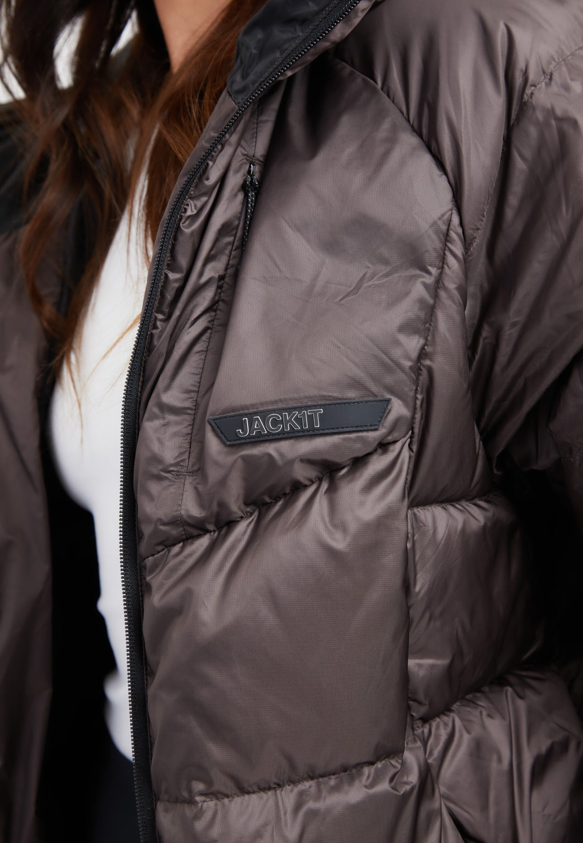 Close-up of an oversized puffer brown jacket featuring a black patch logo on the chest.