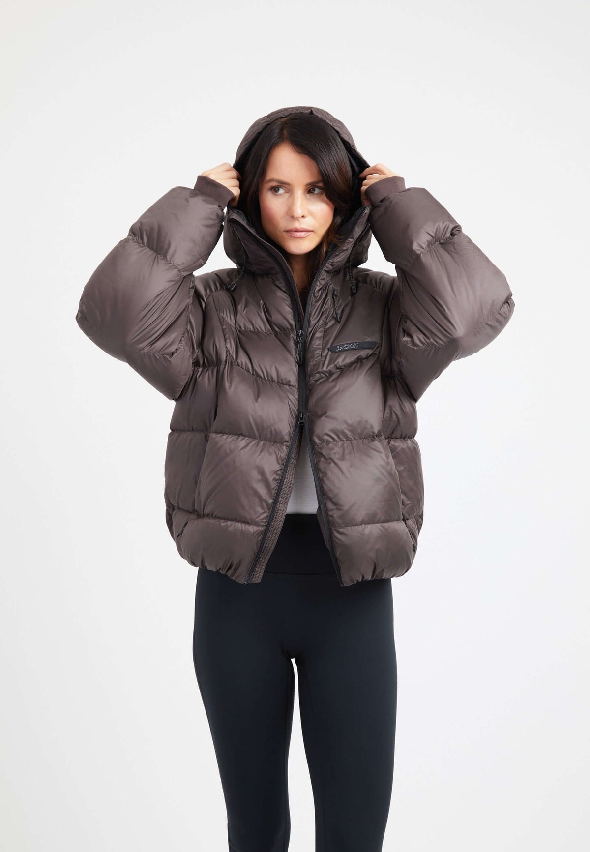 Model wearing an oversized puffer brown bubble jacket with a hood and fleece lined pockets.
