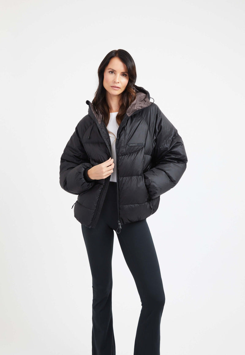 Model wearing an oversized puffer black jacket with adjustable hood and fleece lined pockets.
