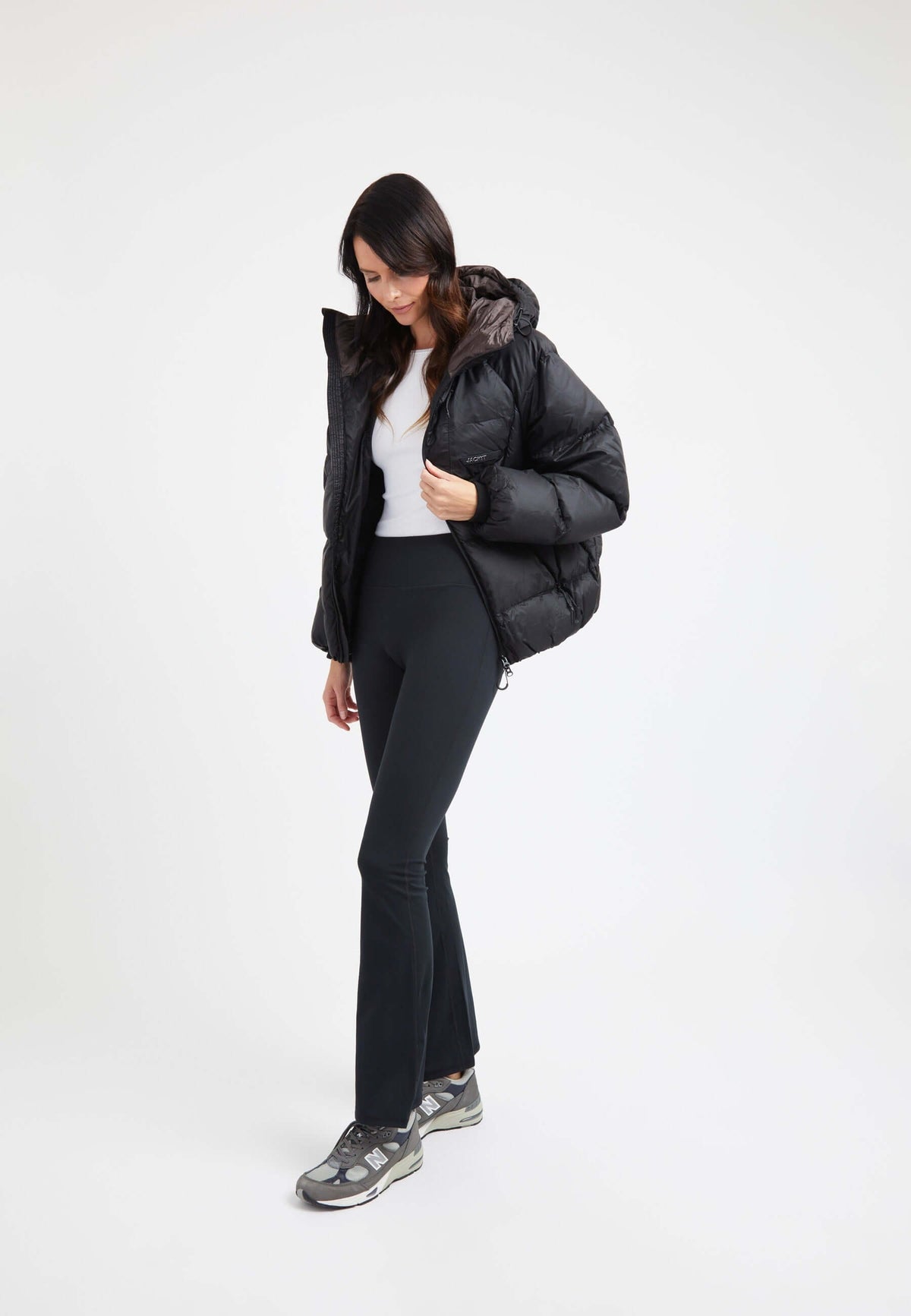 Model wearing an oversized puffer black jacket with a hood, styled with black pants and sporty shoes.