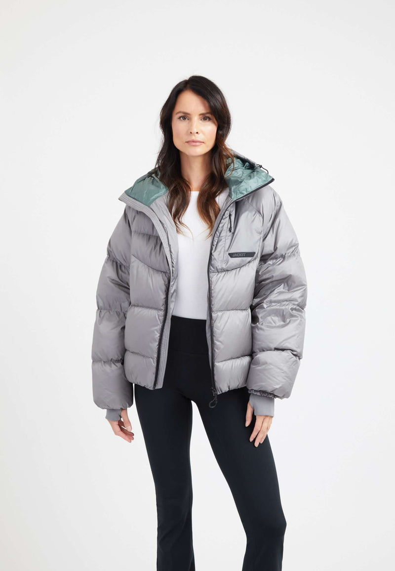 Model wearing an oversized puffer grey jacket with adjustable hood and fleece lined pockets.