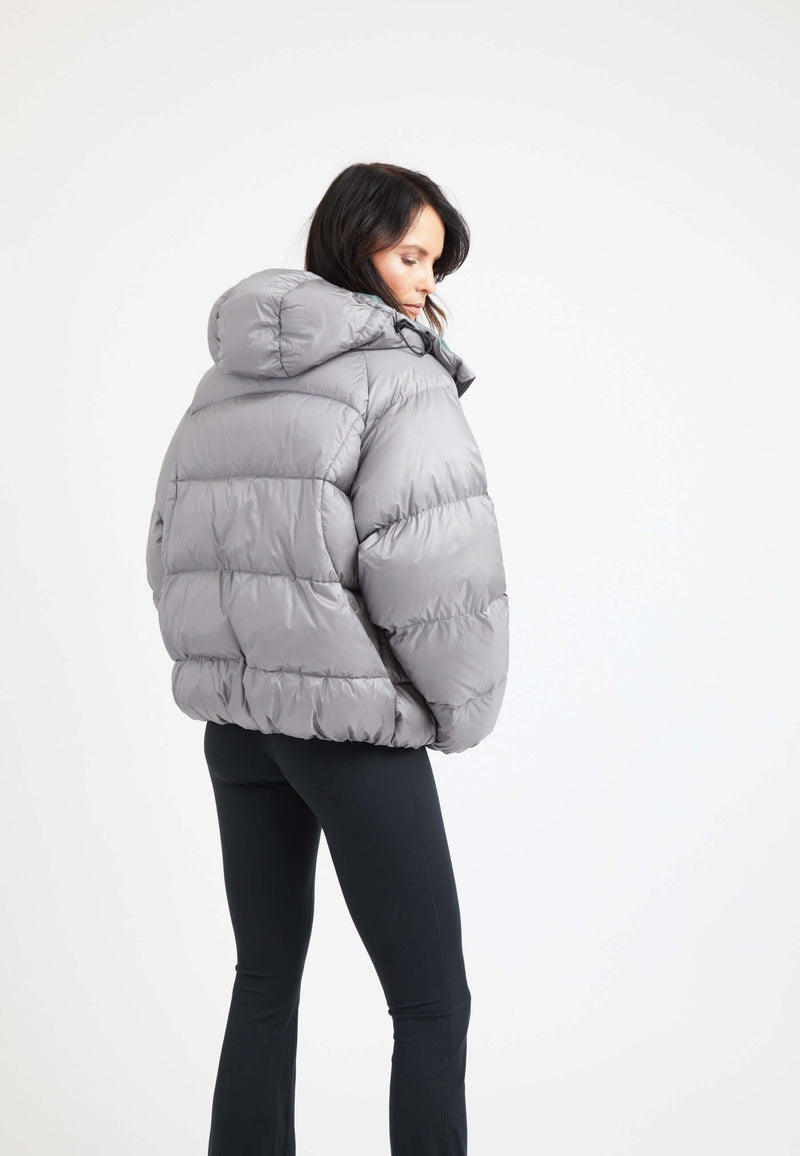 Woman showcasing oversized puffer grey jacket with hood, back view against a plain background.