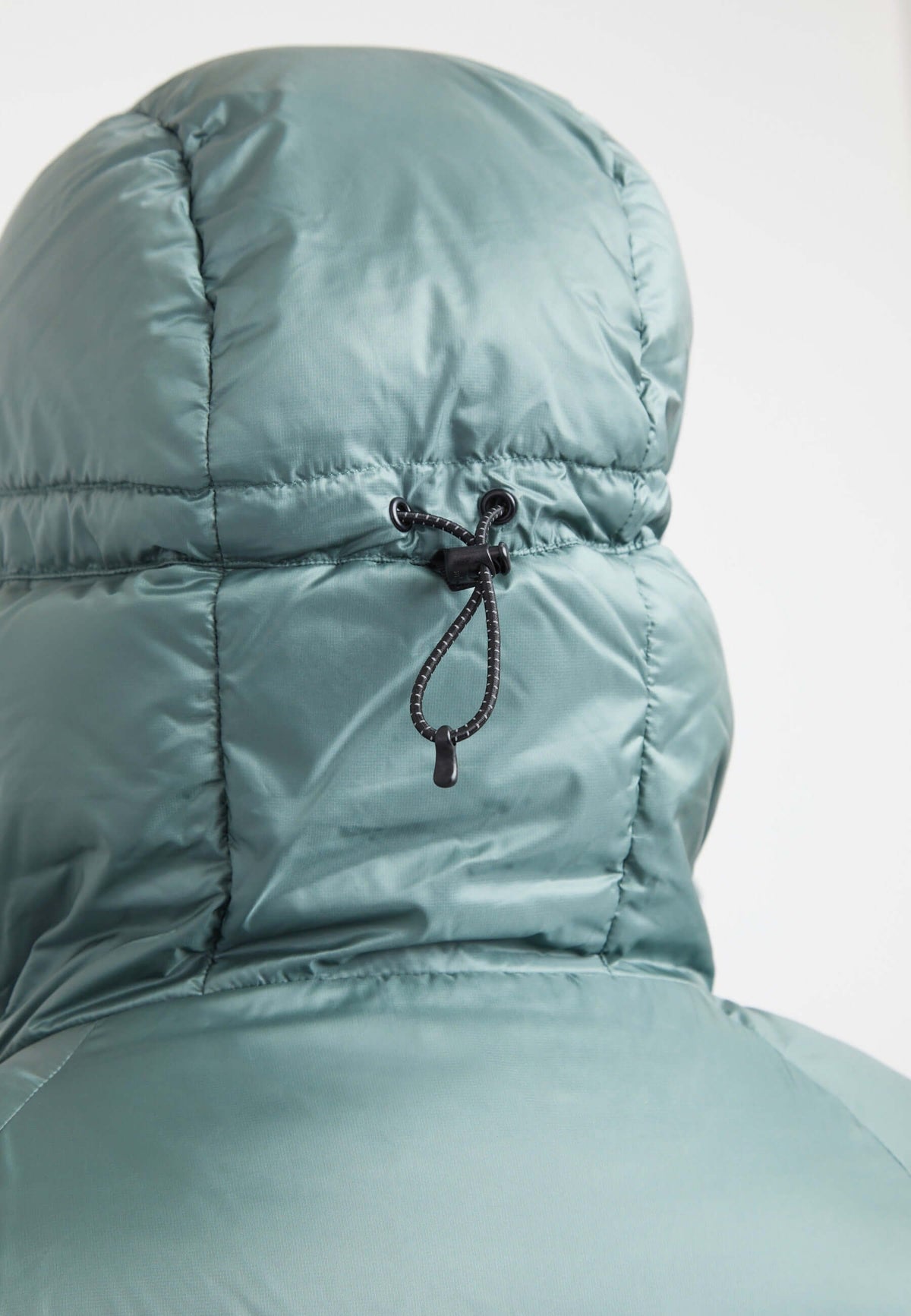 Detail of the adjustable hood on an oversized puffer green jacket, showcasing the fabric and drawstring.