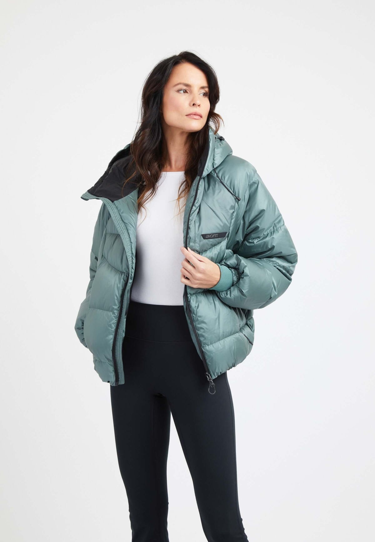 Model wearing an oversized puffer green jacket styled with black leggings and a white top against a plain background.