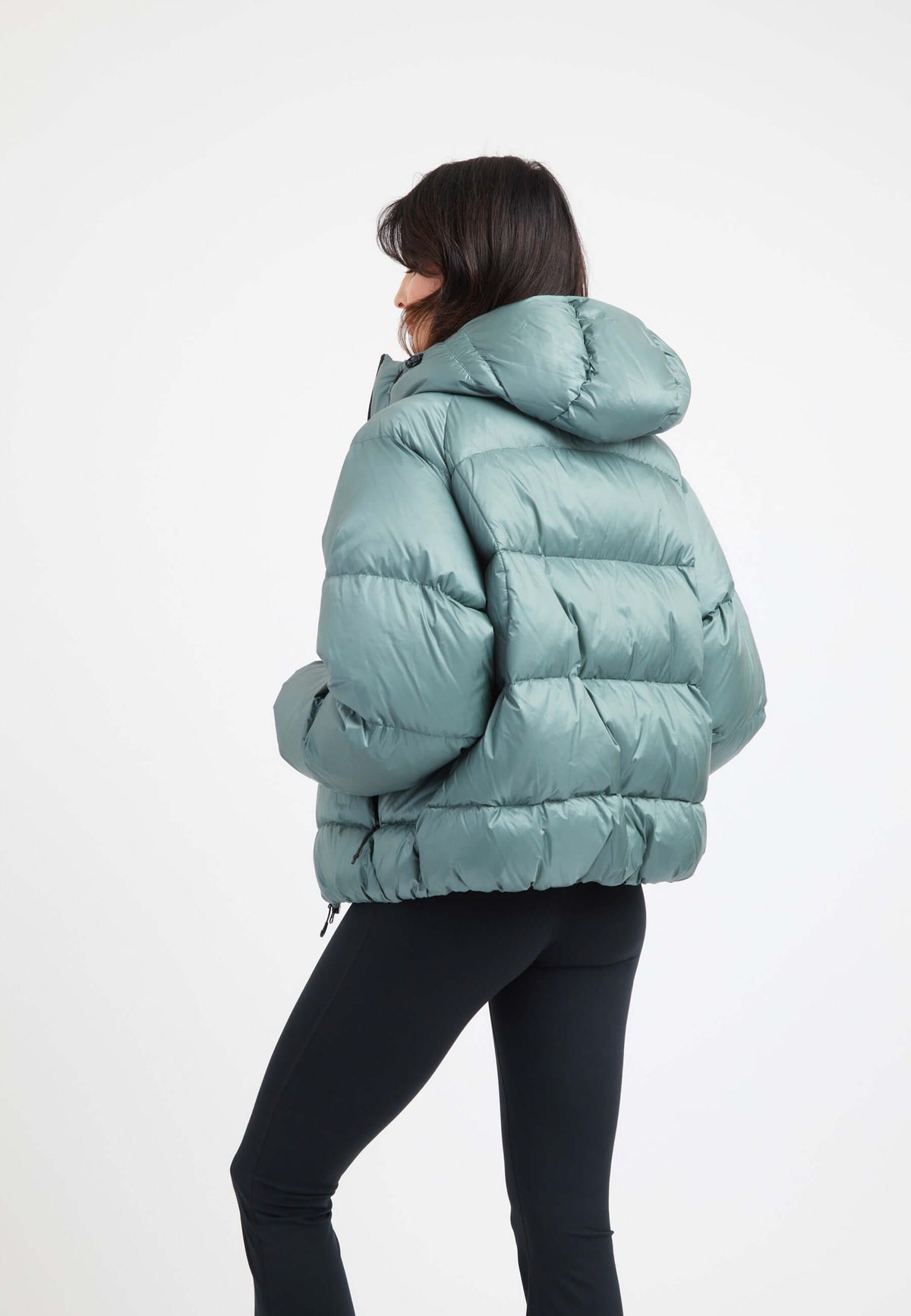 Woman wearing an oversized puffer green jacket, featuring an adjustable hood and modern silhouette.