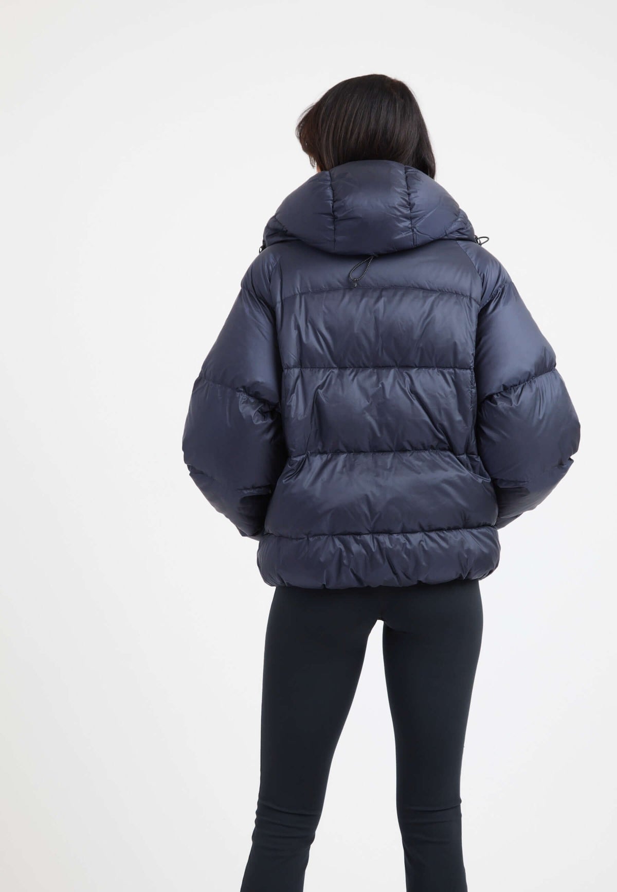 Woman wearing an oversized puffer navy jacket with a hood, showcasing the back view.