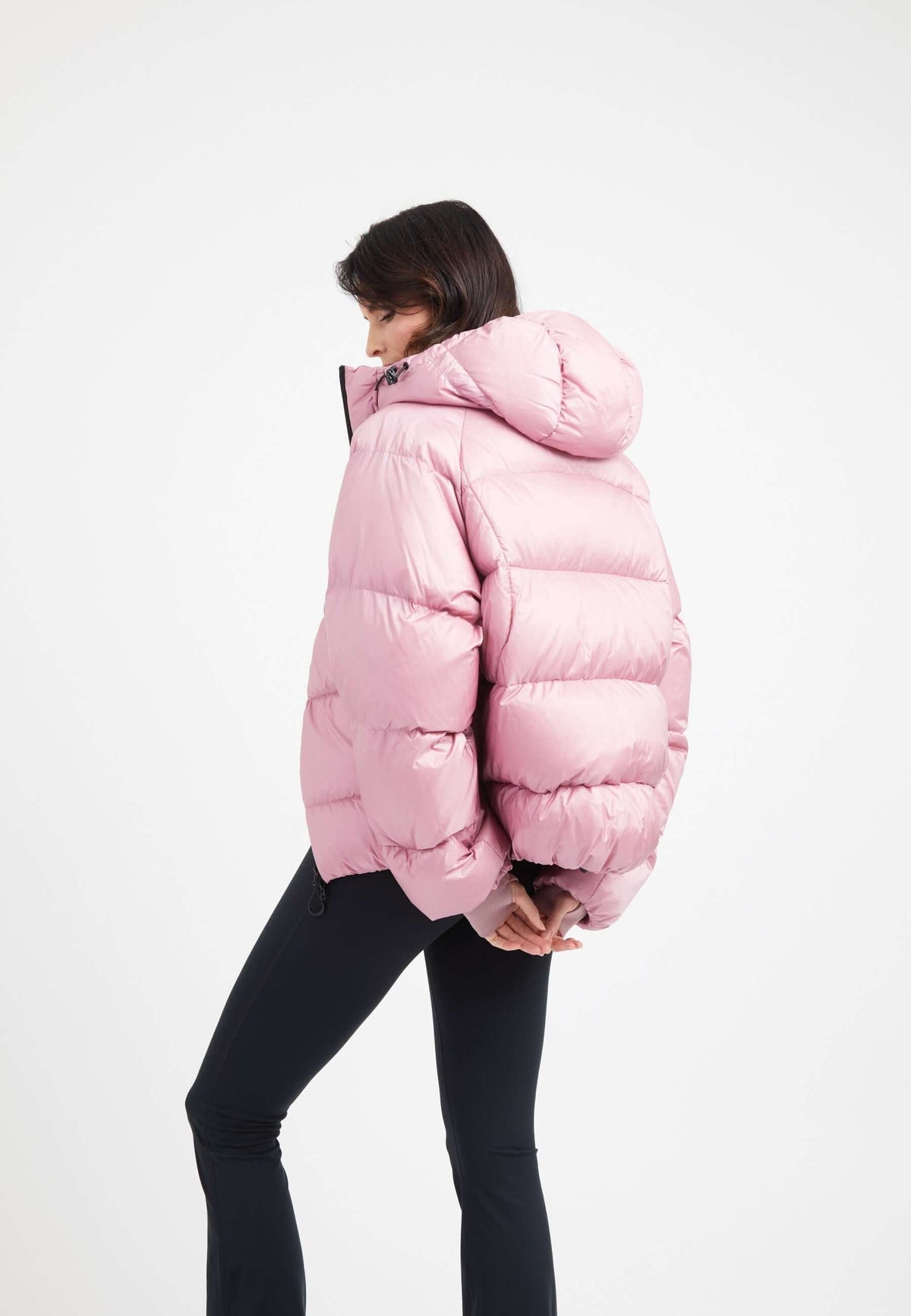 Woman wearing an oversized puffer pink jacket with a hood, showcasing its modern and stylish design.