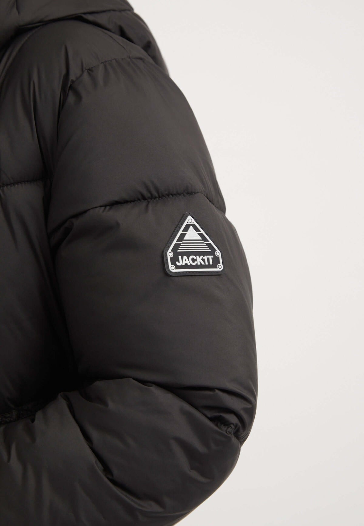Close-up of the sleeve of a black extra long puffer coat featuring JACKIT logo patch.