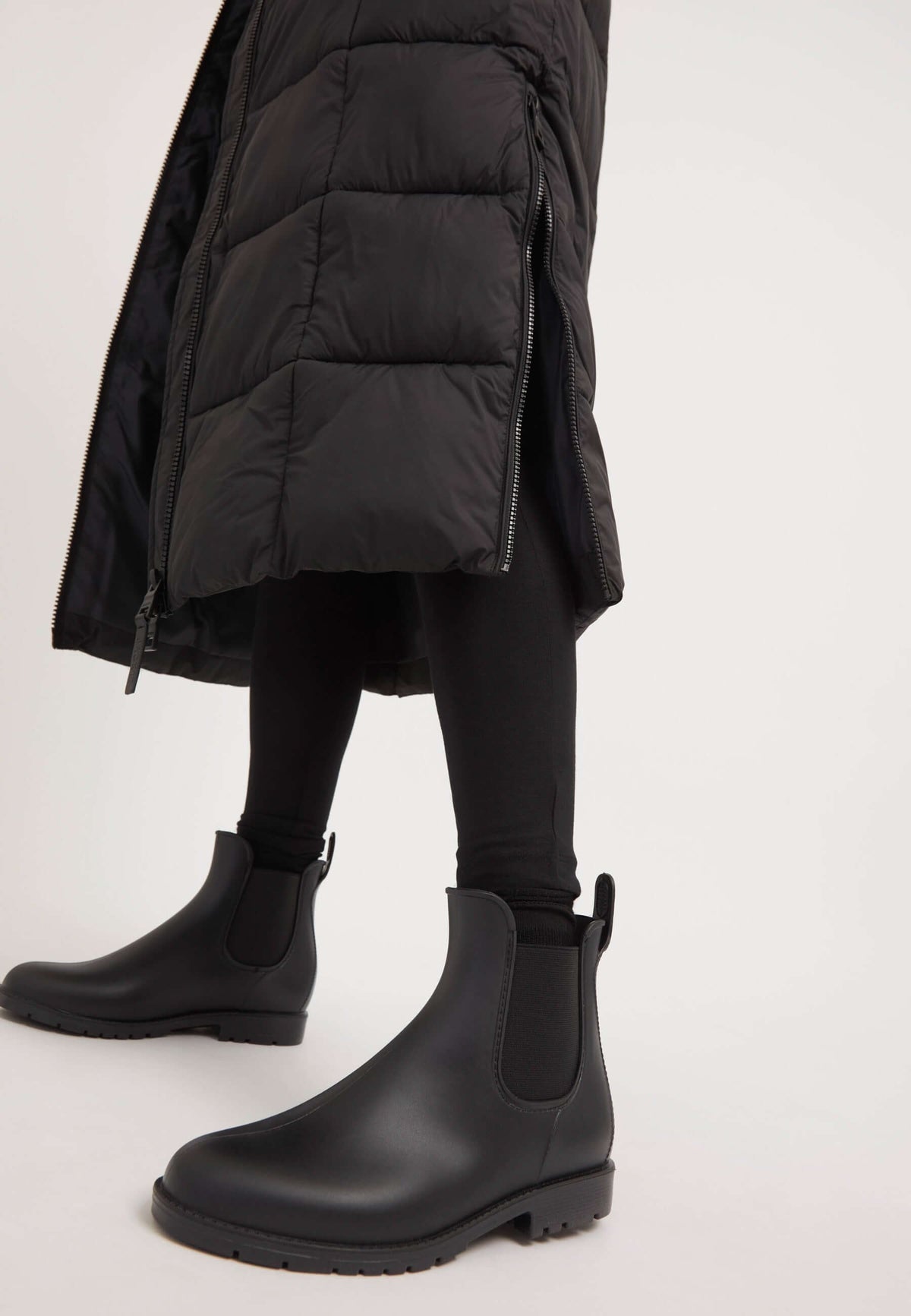 Woman wearing a Black Star extra long puffer coat with side opening and stylish black boots.