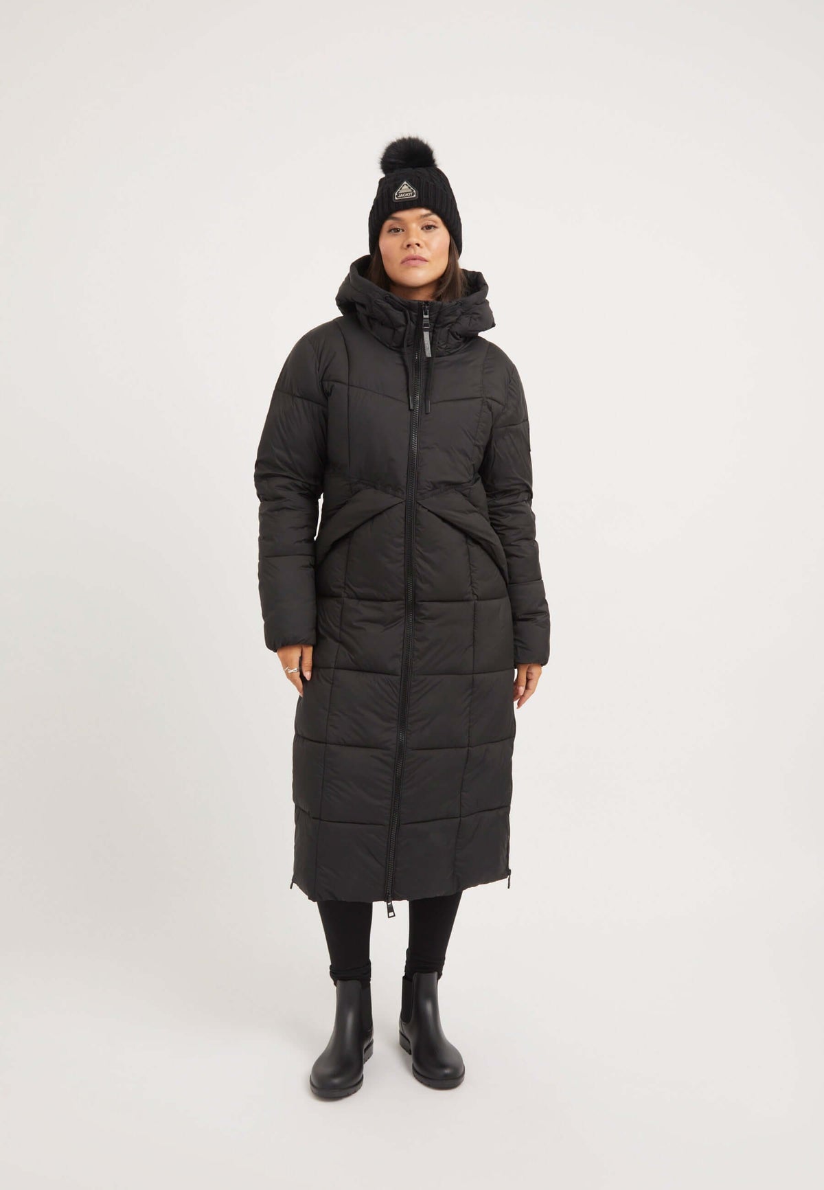 Model wearing extra long puffer coat in black with hood, side openings, and two-way zips, showcasing stylish winter outerwear.