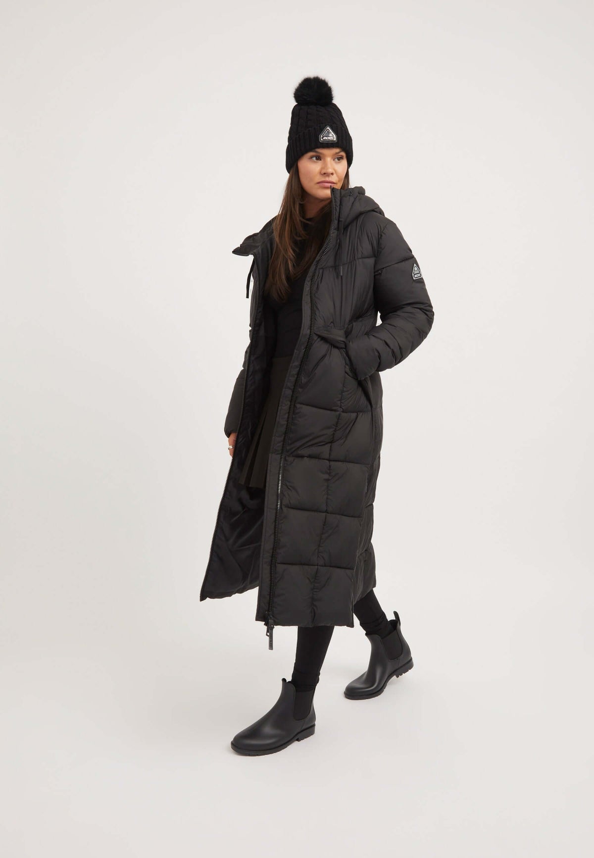 Woman wearing a Black Star extra long puffer coat, styled with a beanie and black boots, showcasing a full length silhouette.