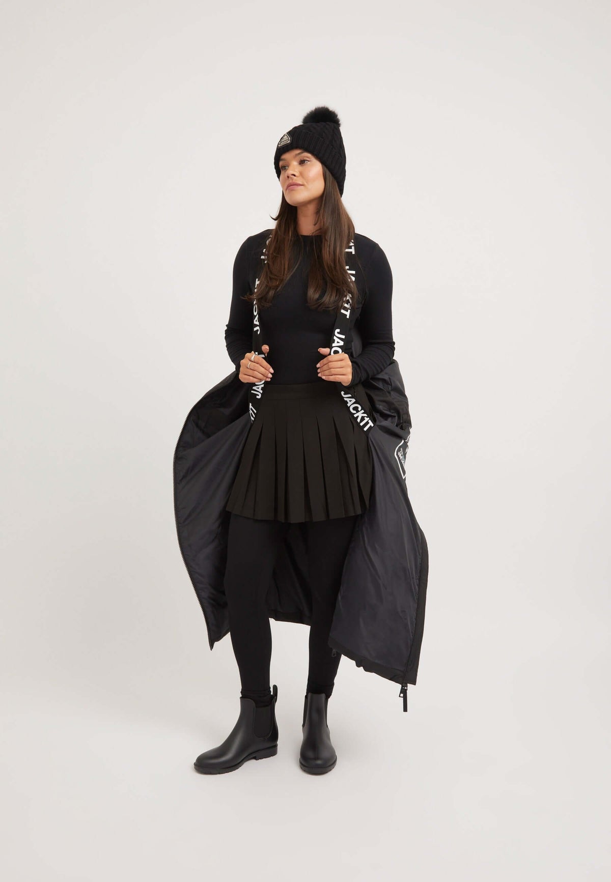 Model wearing a black star ex-long puffer coat with a black pleated skirt and beanie, showcasing an extra long puffer coat style.