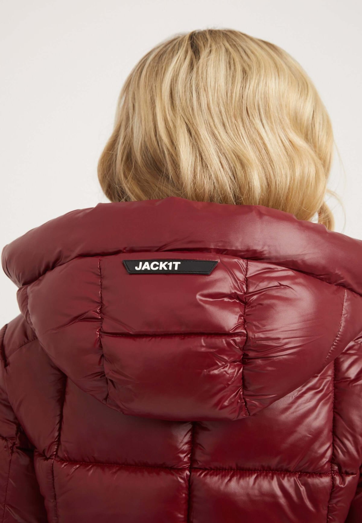 Back view of woman wearing EZ Box Crop Jacket Dark Cranberry, a short puffer jacket women with a hood and JACKIT logo.