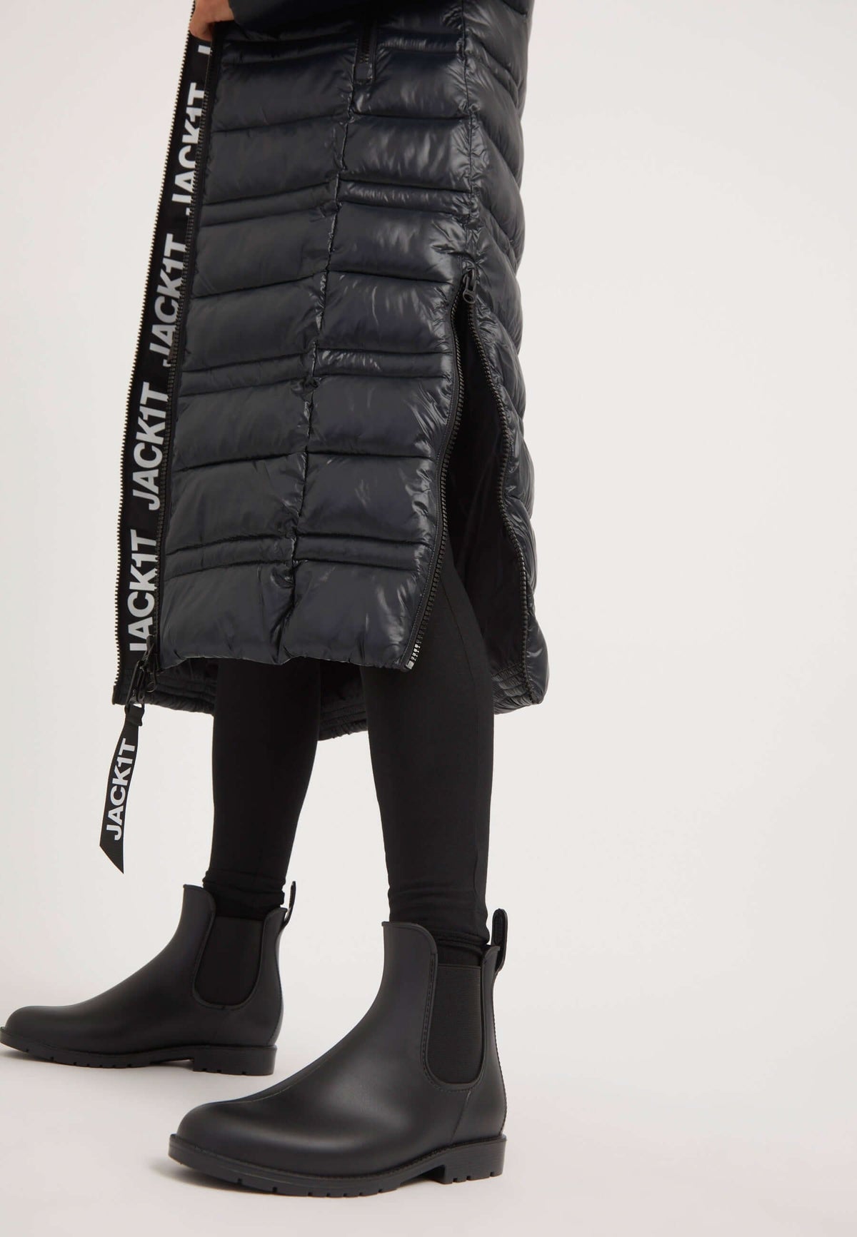 Person wearing an R4D Extra Long Puffer Coat with black ankle boots, showcasing the coat's side slit opening.