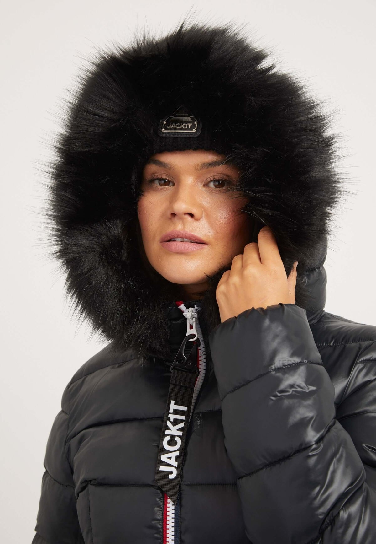 Woman wearing a black womens puffer jacket with removable faux-fur trim and reflective badge, stylish winter outerwear.
