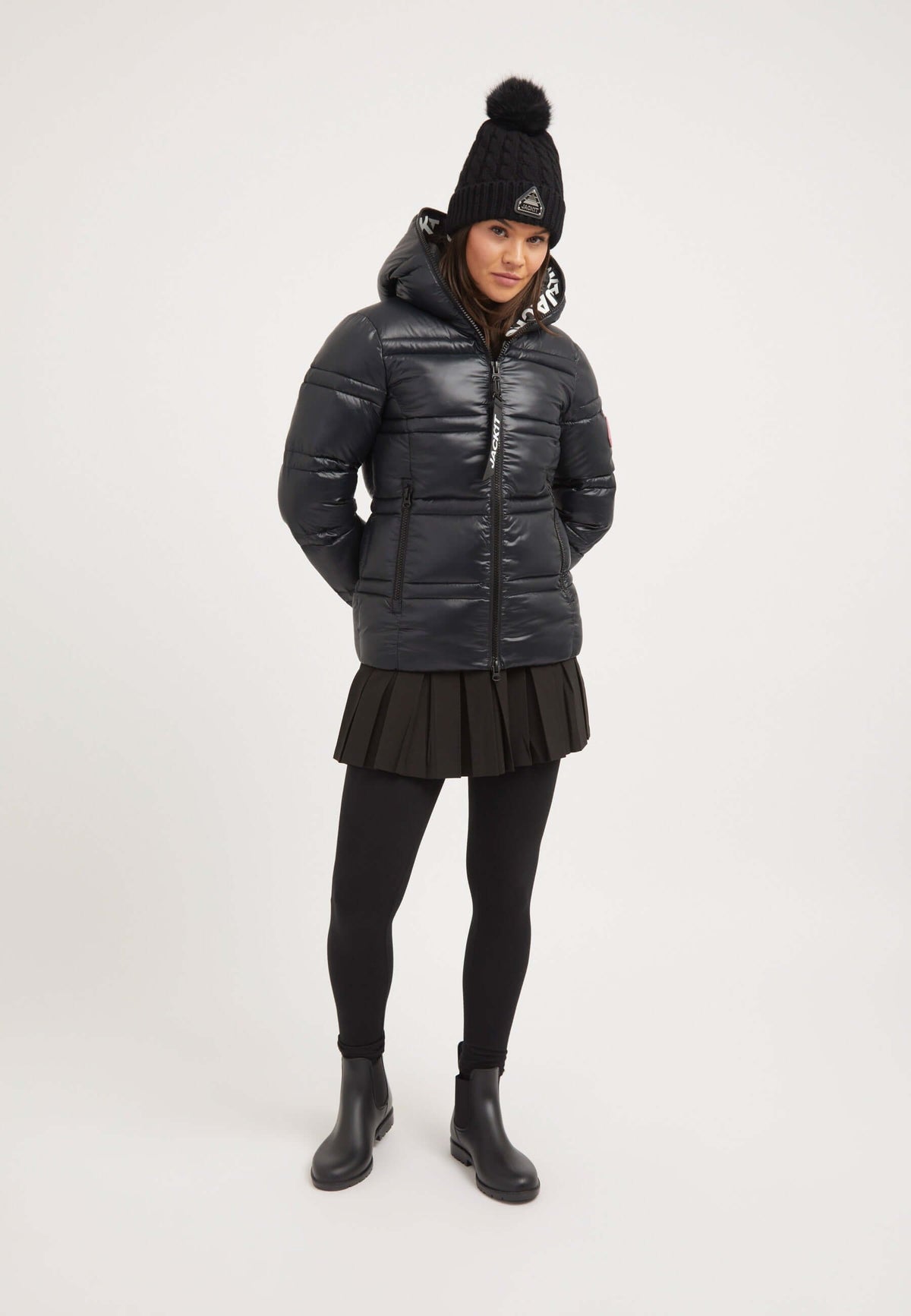 Model wearing R4D Tramline Racer Jacket Black, a ladies black puffer jacket, styled with a skirt and hat.