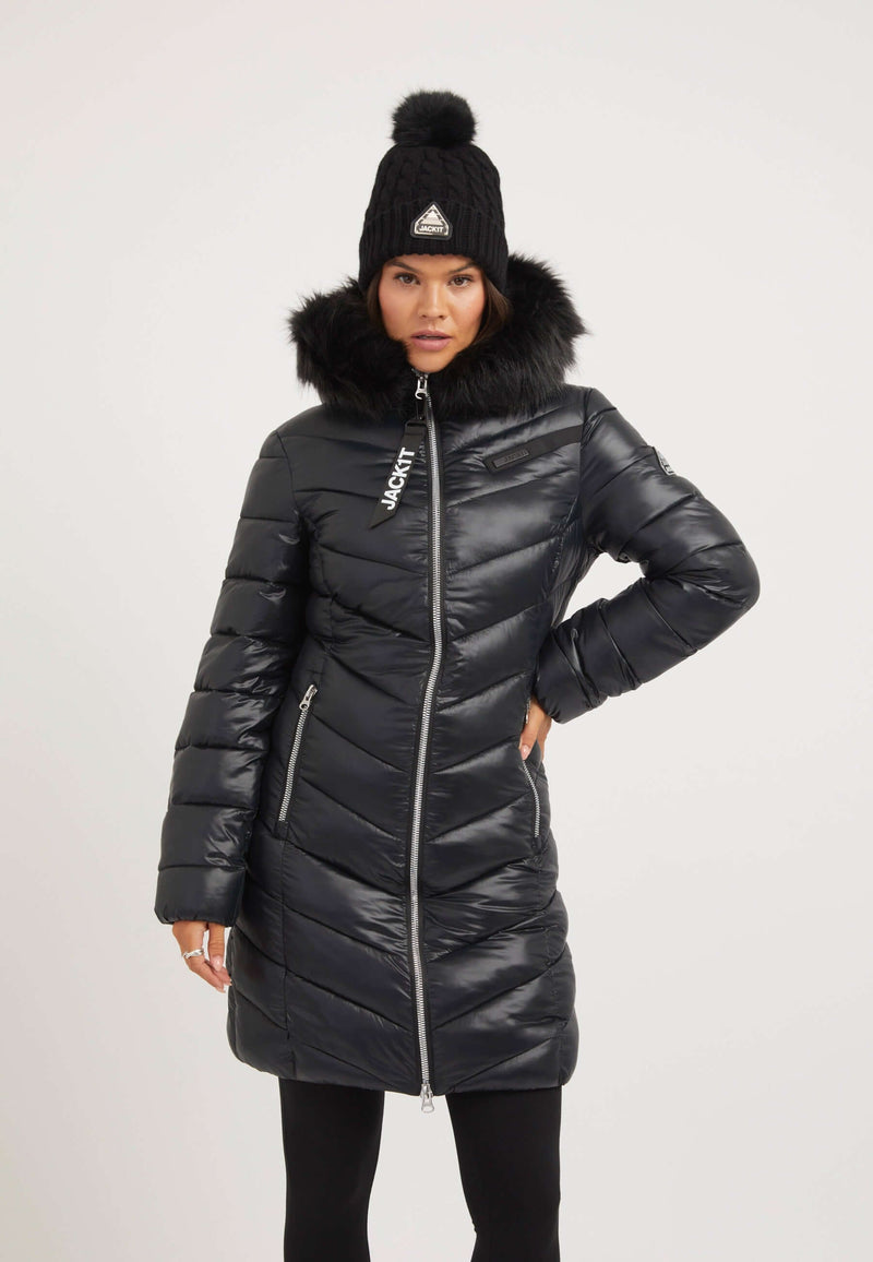 Model wearing the R4D Luxe Coat Black, a black womens puffer coat with faux-fur hood and two way zips.