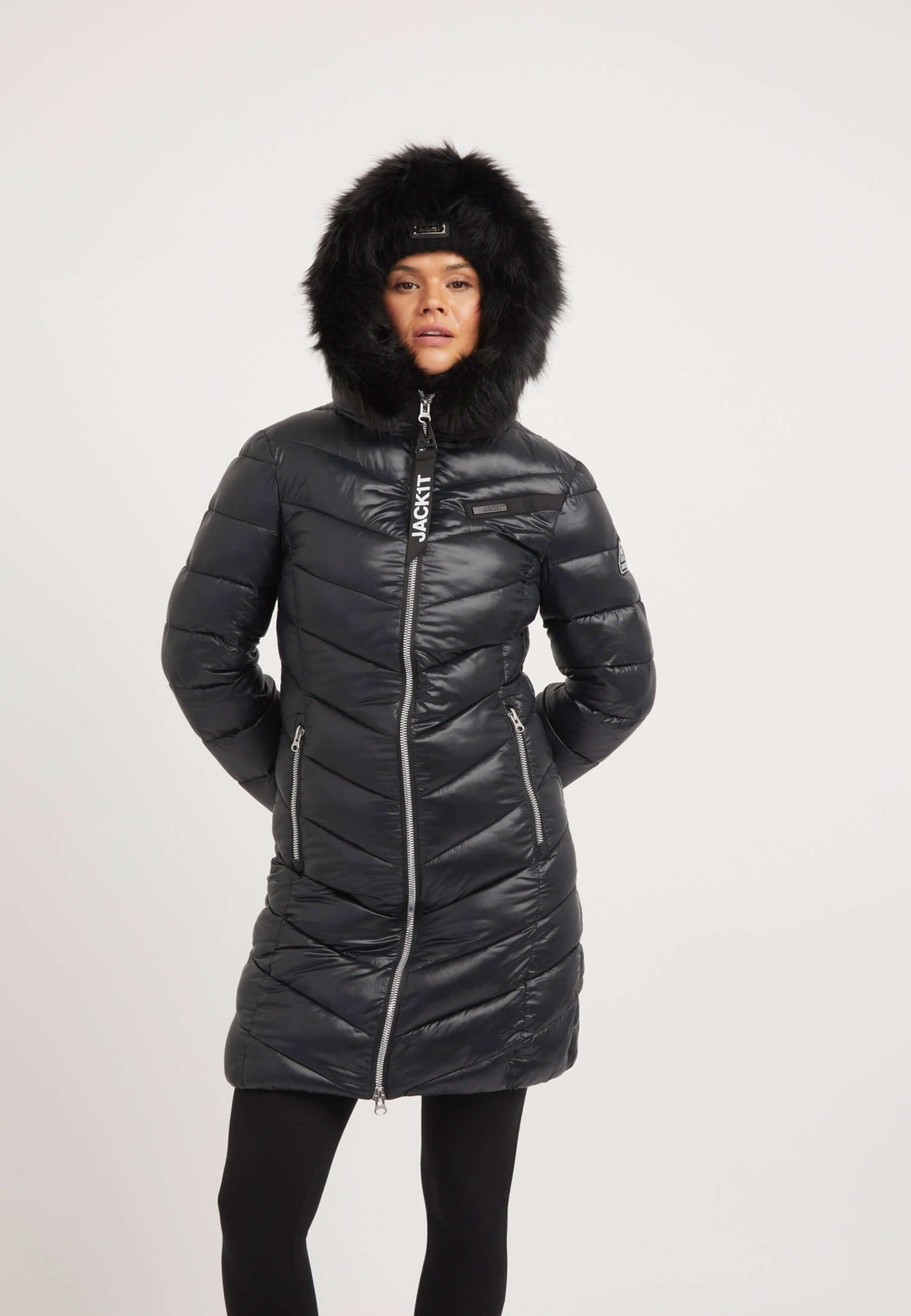 Model wearing R4D Luxe Coat Black, a black womens puffer coat with faux-fur hood and zippered pockets.