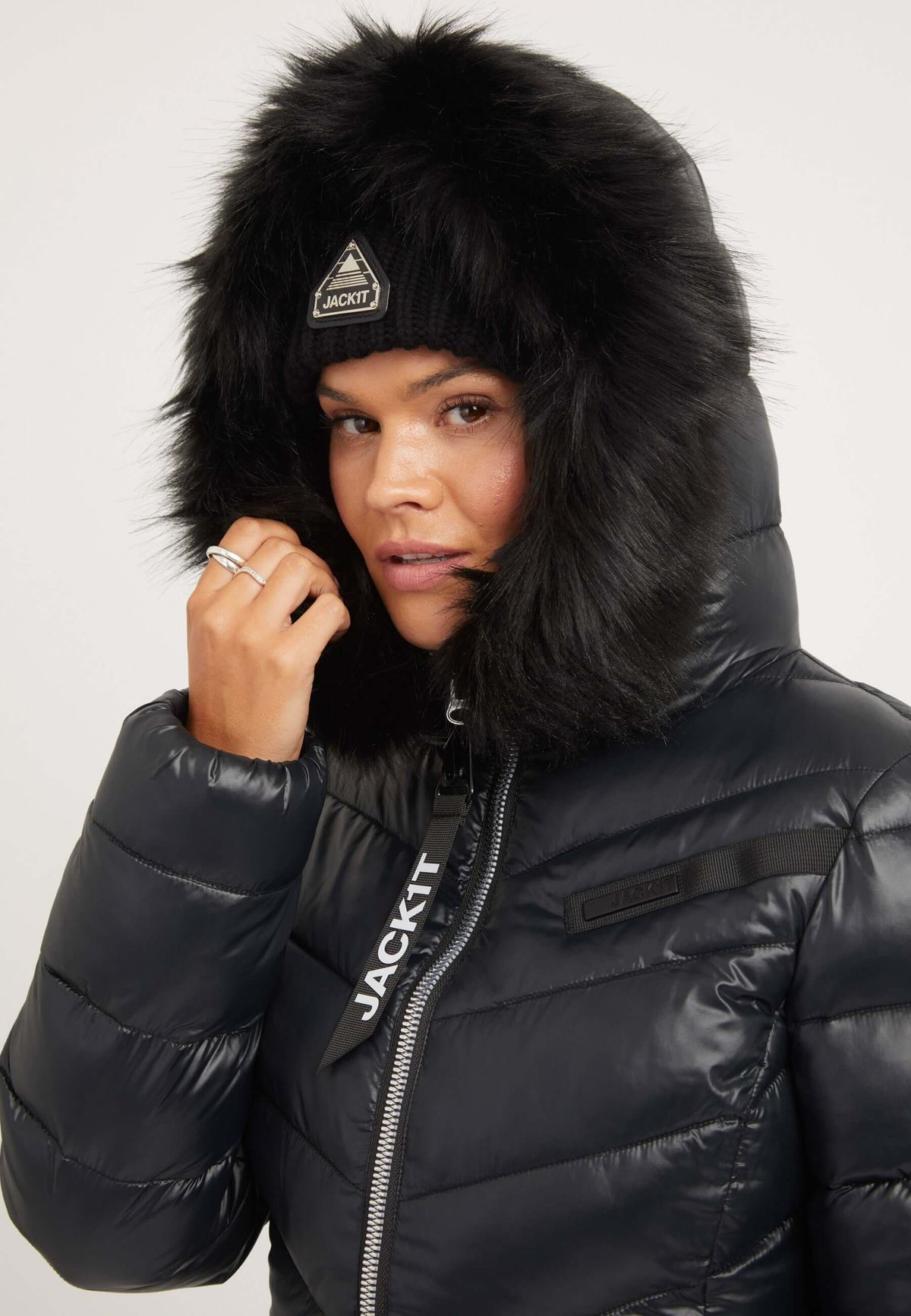 Model wearing a R4D Luxe Coat Black with faux-fur hood and reflective badge, showcasing a stylish black womens puffer coat.