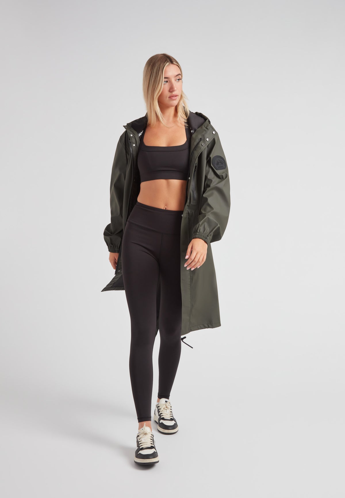 Model wearing ELEMENTS unisex raincoat in khaki over black activewear, showcasing stylish outdoor wear.