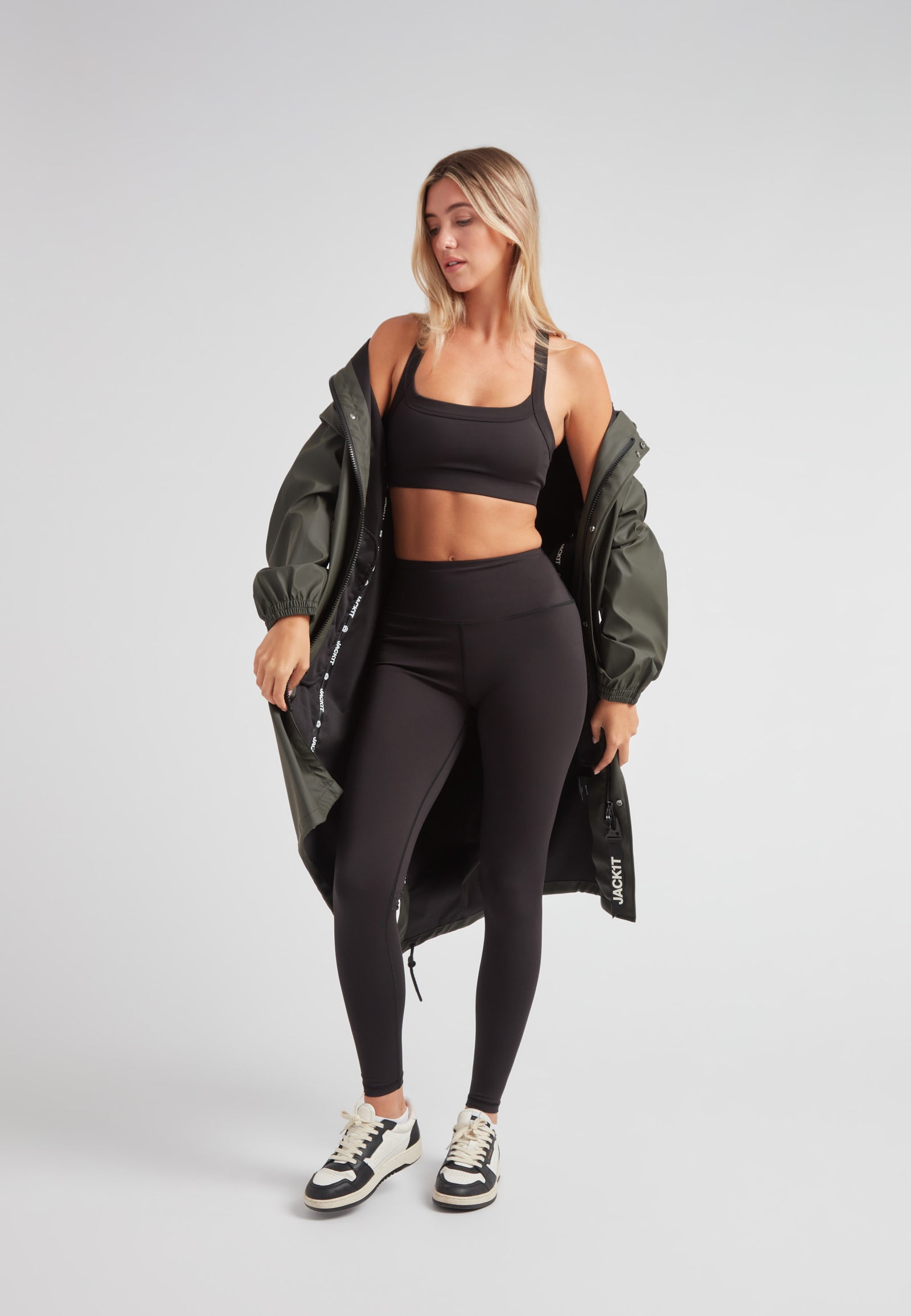 Model wearing ELEMENTS unisex raincoat in khaki with black leggings and crop top.
