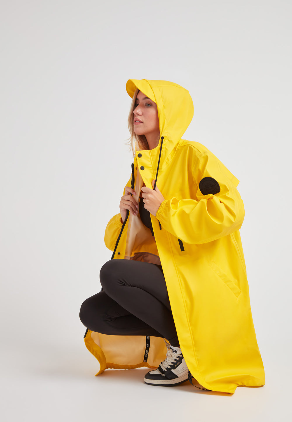 A model wearing a yellow ELEMENTS longline raincoat 2.0, showcasing its lightweight and stylish design.