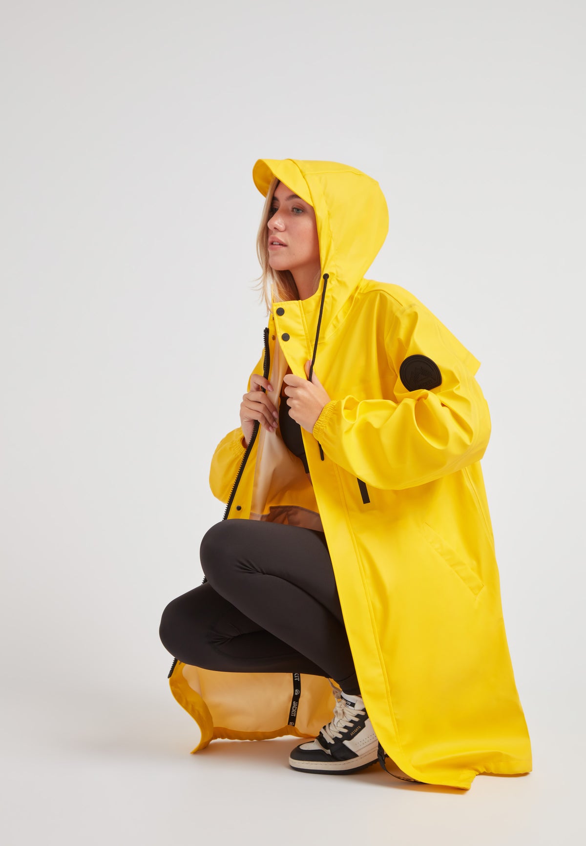 A model wearing a yellow ELEMENTS longline raincoat 2.0, showcasing its lightweight and stylish design.