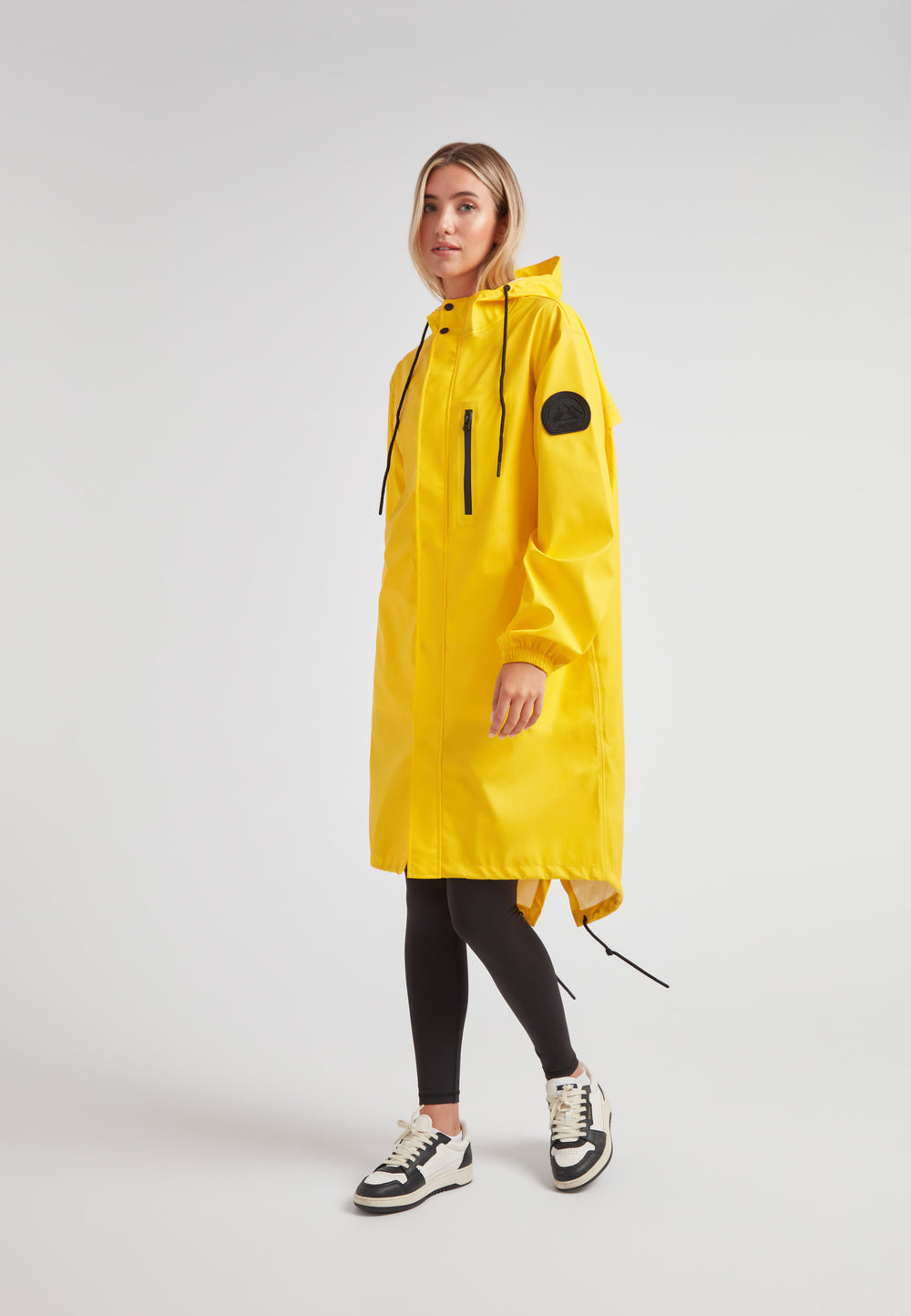 Model wearing a yellow Elements longline raincoat, featuring a hood and adjustable drawstrings for a stylish, waterproof look.