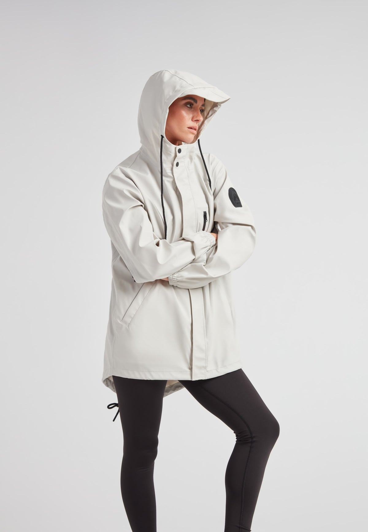 Woman wearing ELEMENTS Raincoat 2.0 Stone with hood, showcasing stylish weather protection.