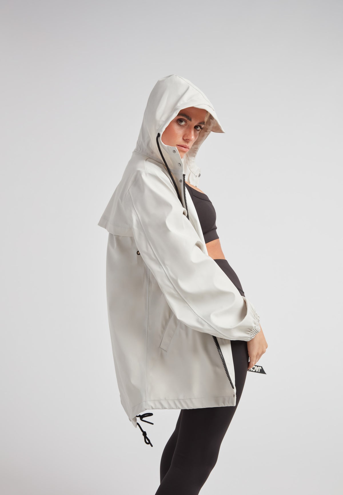 Woman wearing the ELEMENTS Raincoat 2.0 Stone with a hood, showcasing its lightweight design.