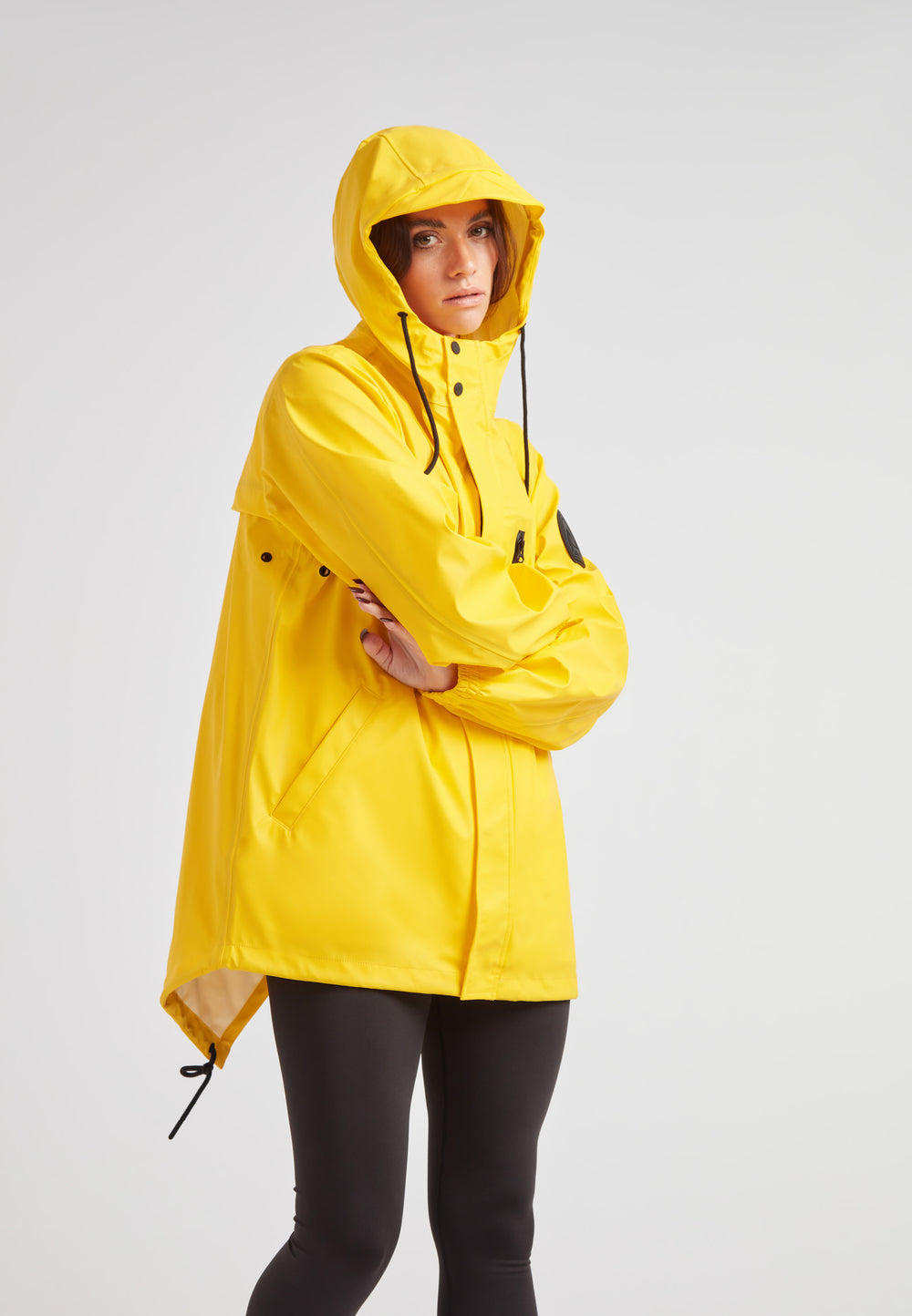 Model wearing ELEMENTS Raincoat 2.0 Yellow with hood, showcasing its lightweight and stylish design.