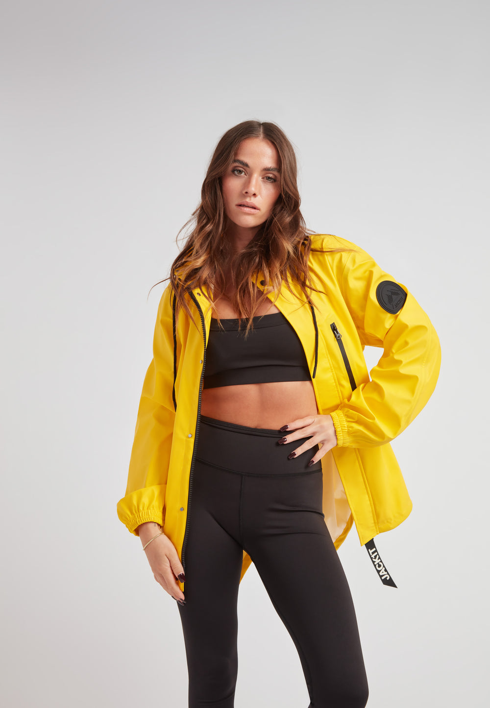 Model wearing ELEMENTS Raincoat 2.0 Yellow with black athleisure outfit, showcasing stylish design and functionality.