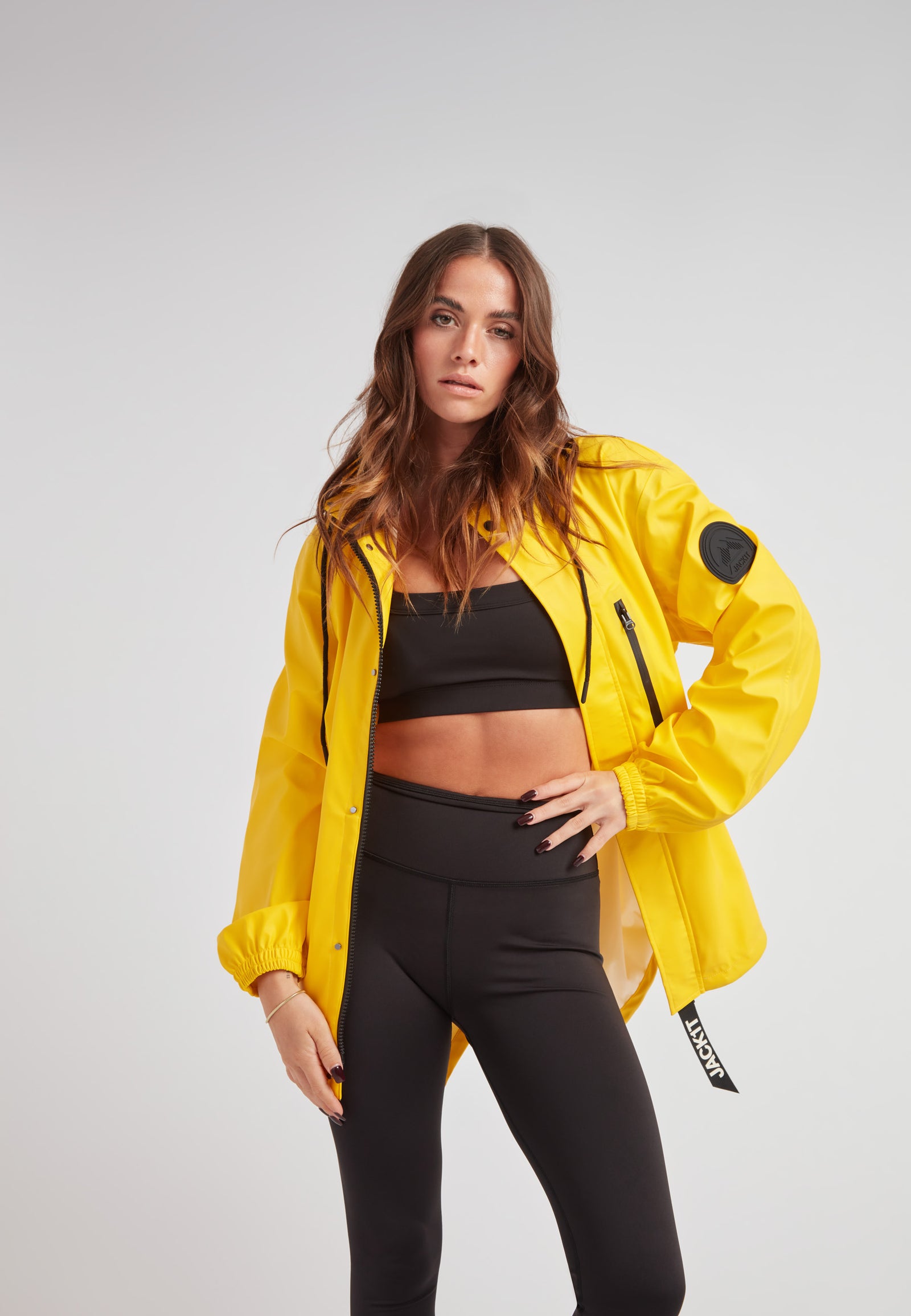 Model wearing ELEMENTS Raincoat 2.0 Yellow with black athleisure outfit, showcasing stylish design and functionality.