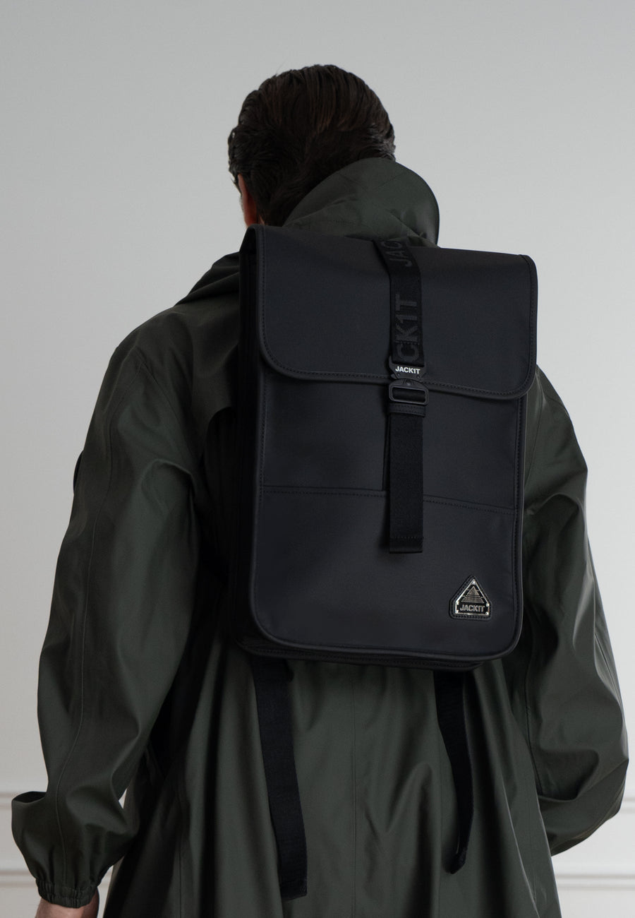 The JACK1T slim messenger laptop bag in black worn on the back of a person with a green coat.