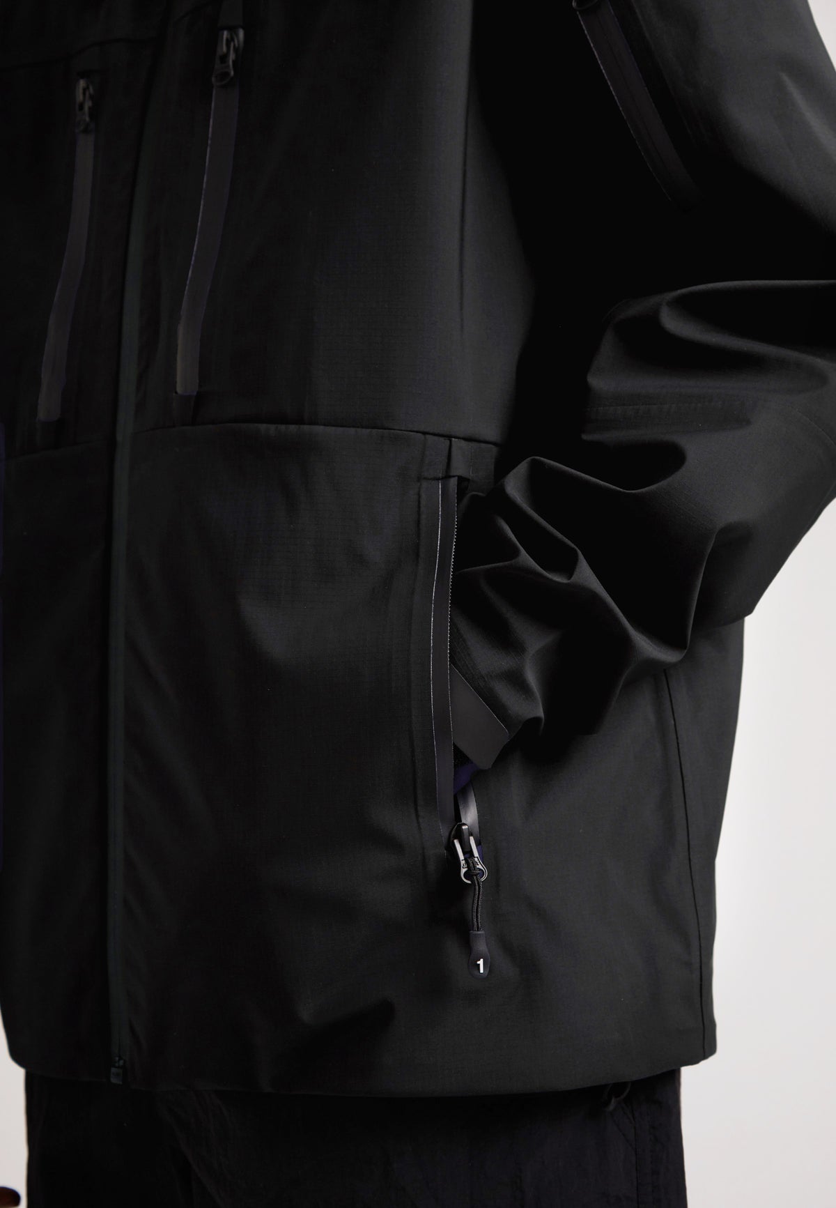 Black mens Lithium waterproof jacket showcasing a close-up of the zippered pockets and durable design.