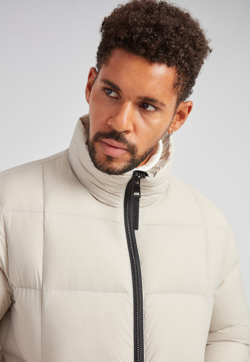 Model wearing the Cloud Lightweight Puffer Racer Jacket Stone with a funnel neck and box quilting.