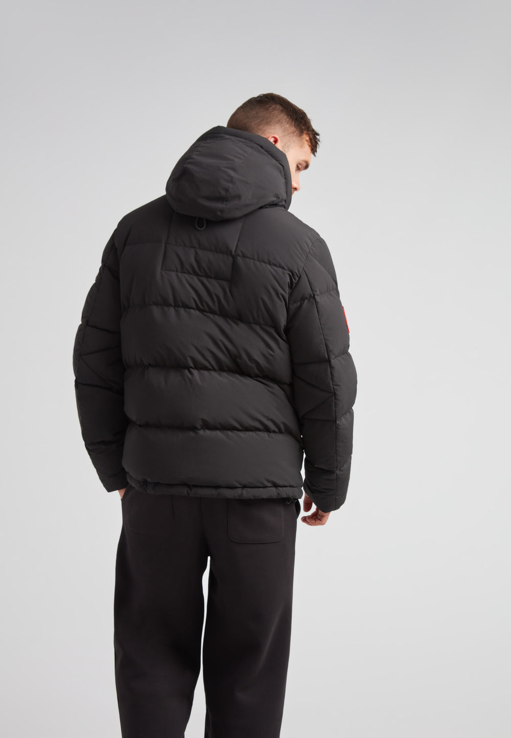 Back view of a model wearing the EZ Frontier Prime Down Puffer Jacket Matt Black, featuring a hood and puffer design.