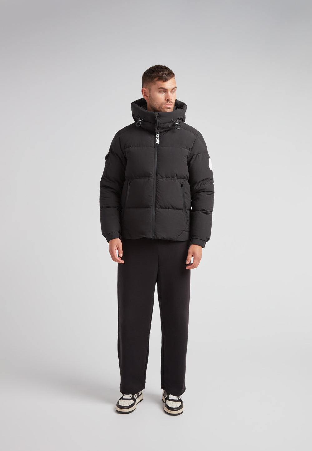EZ Water Puffer Racer Jacket Matt Black worn by a man standing with a grey background, showing a stylish winter look.