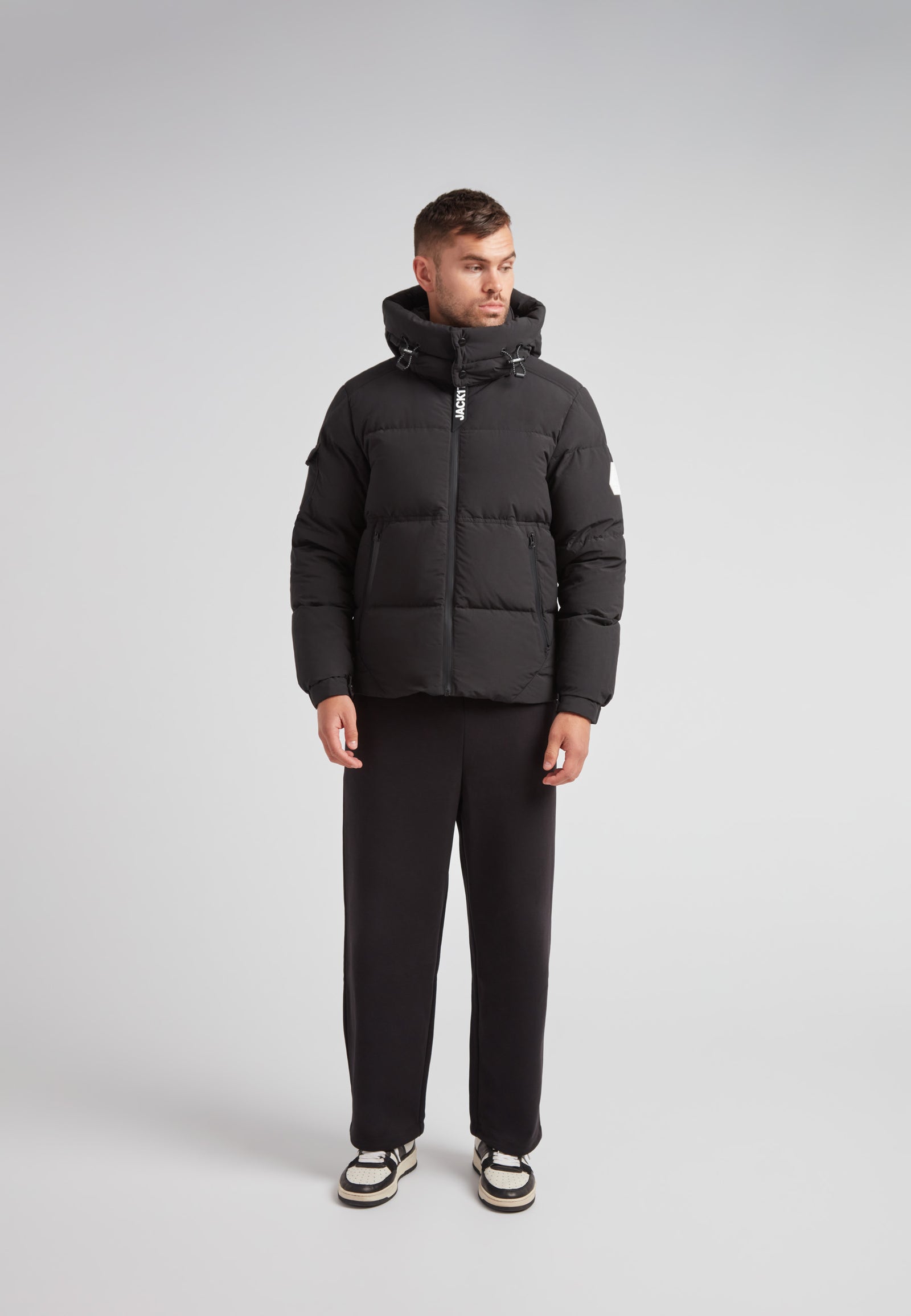 EZ Water Puffer Racer Jacket Matt Black worn by a man standing with a grey background, showing a stylish winter look.