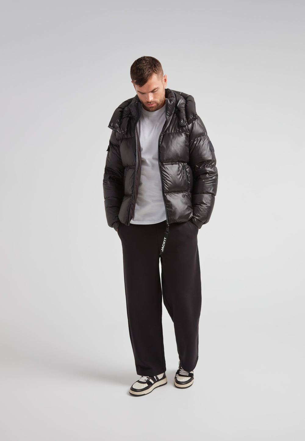Man wearing EZ Water Puffer Racer Jacket Lux Black with stylish gray shirt and black pants, showcasing active winter fashion.