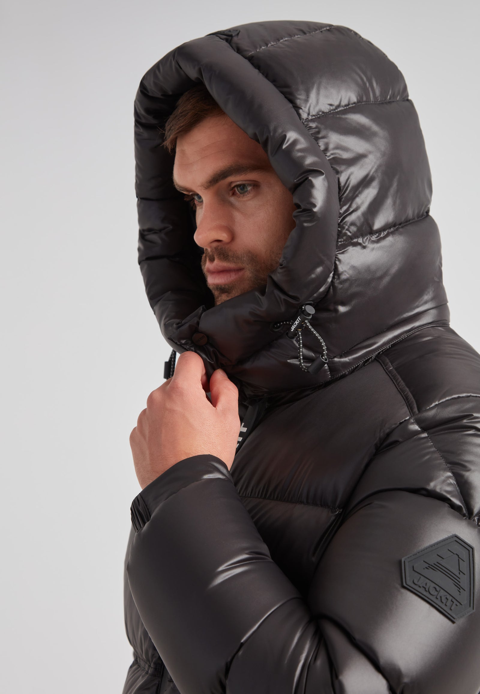 Man wearing the EZ Water Puffer Racer Jacket Lux Black with hood up, showcasing a sleek design and modern look.